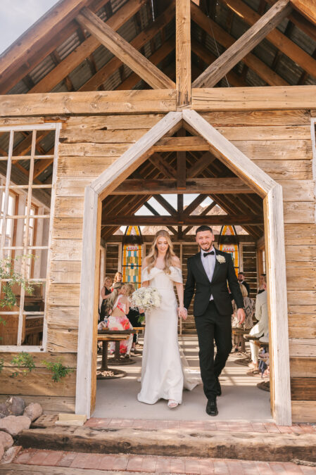 bride and groom walking out of las vegas desert wedding ceremony in wooden chapel with stained glass windows