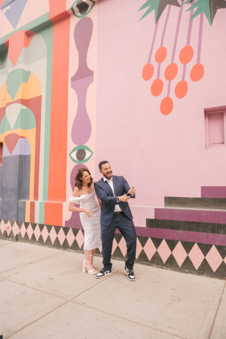 bride and groom popping champagne in front of mural  in downtown las vegas
