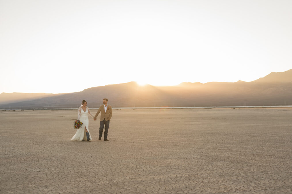 fall elopement bride and groom walking at sunset on dry lake bed
